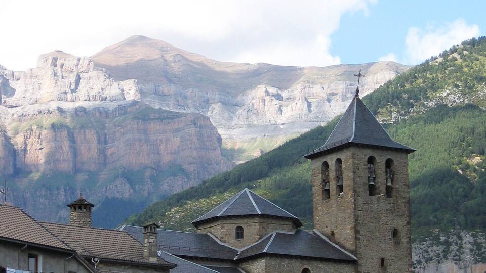 A mountainous landscape with a church featuring a bell tower and a stone building with a tiled roof.