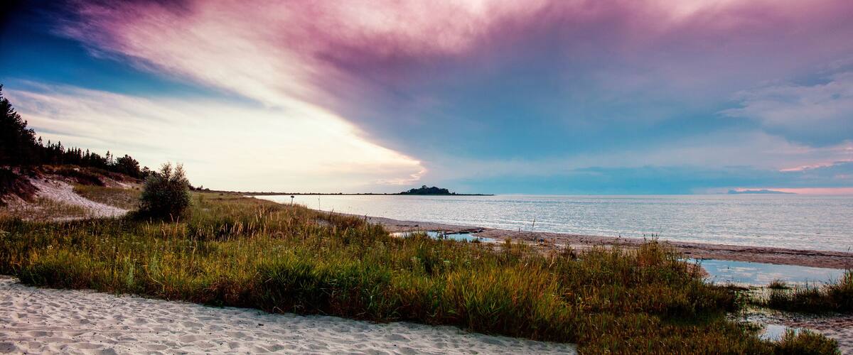 A beach with sand, grass, and a body of water.