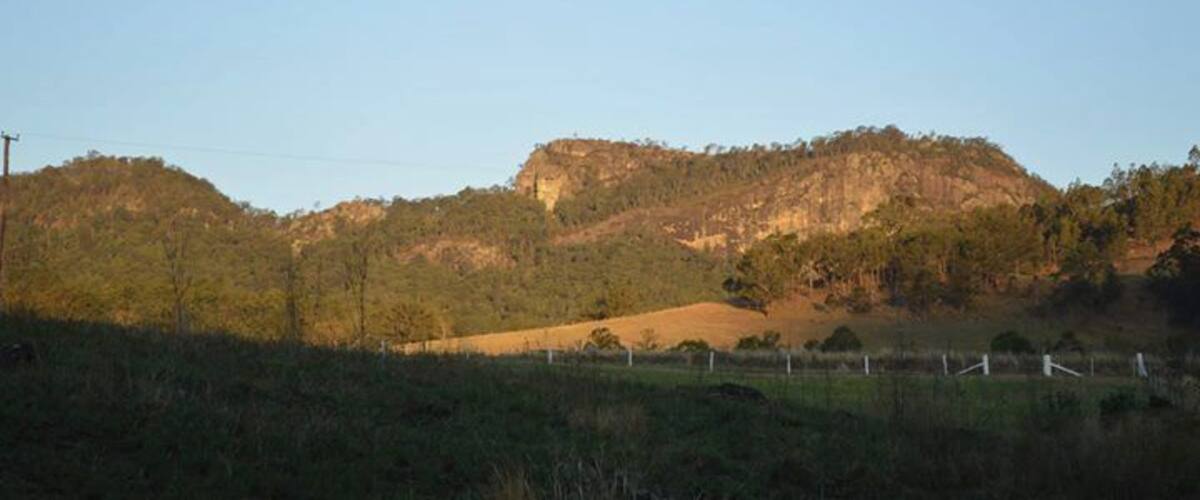 A hilly landscape with a prominent hill in the background and a fence in the foreground.