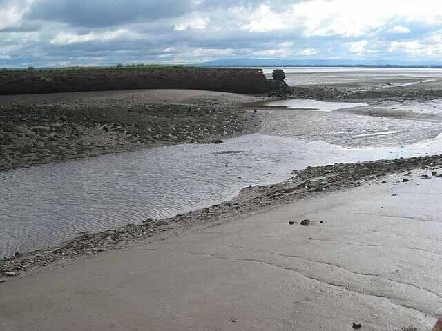 A coastal landscape with a sandy beach, a tidal flat, and a distant rocky outcrop.