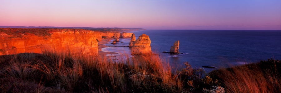 A coastal landscape with rock formations and a beach at sunset.