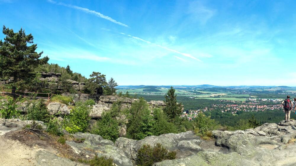 A rocky mountain landscape with a cross, a trail, and a distant town.