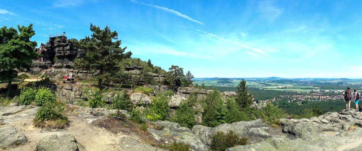 A rocky mountain landscape with a cross, a trail, and a distant town.