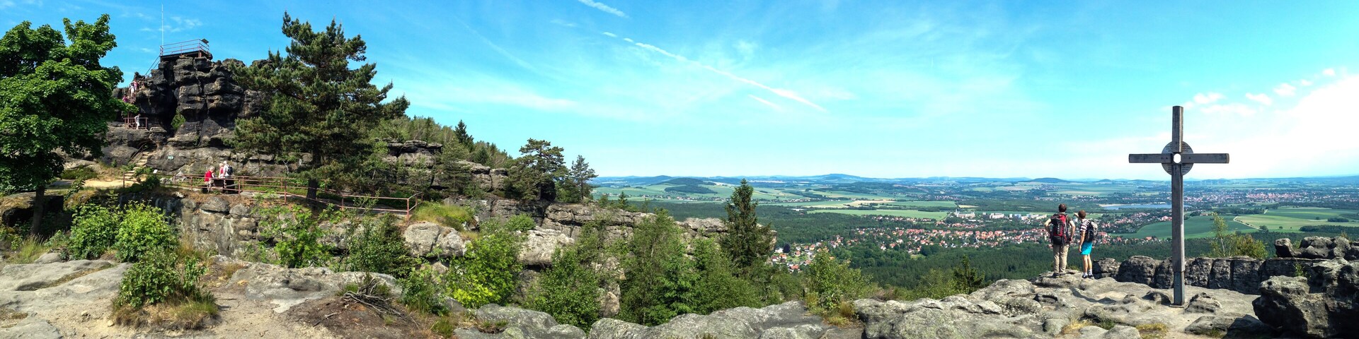 A rocky mountain landscape with a cross, a trail, and a distant town.