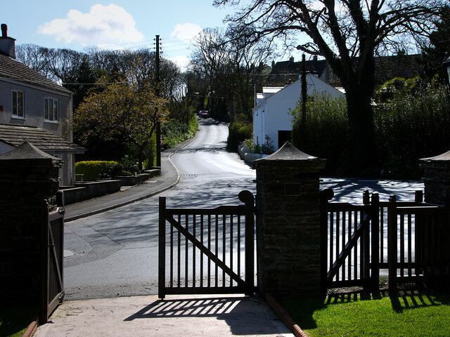 A residential street with houses, a gated driveway, and a clear sky.