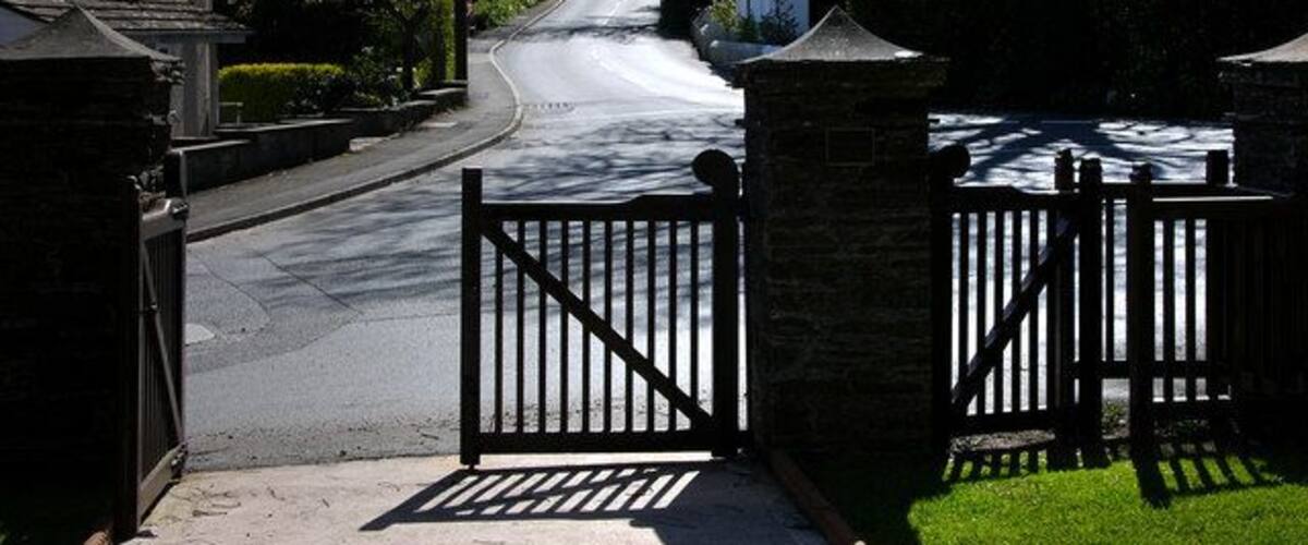 A residential street with houses, a gated driveway, and a clear sky.