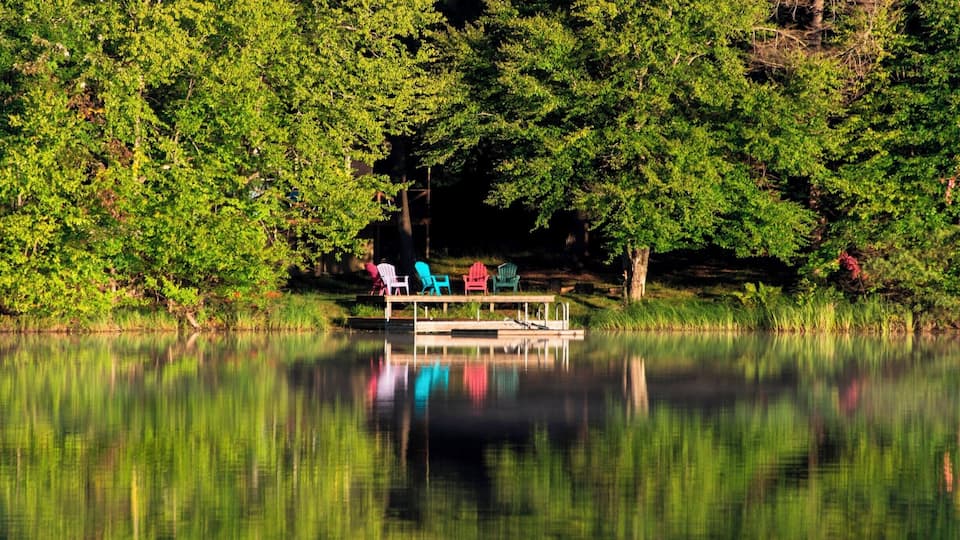 A calm lake with a dock and colorful chairs.