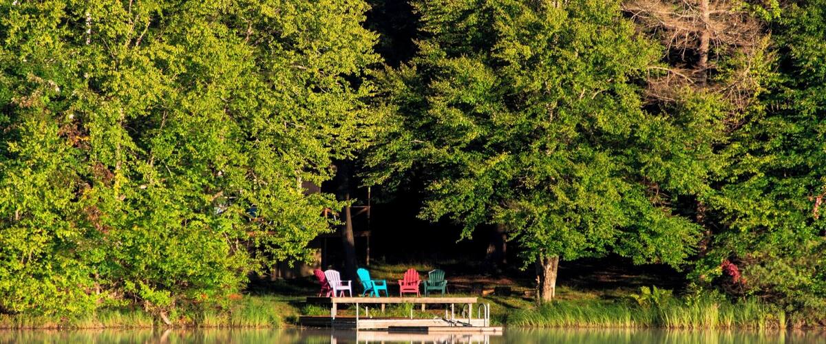 A calm lake with a dock and colorful chairs.