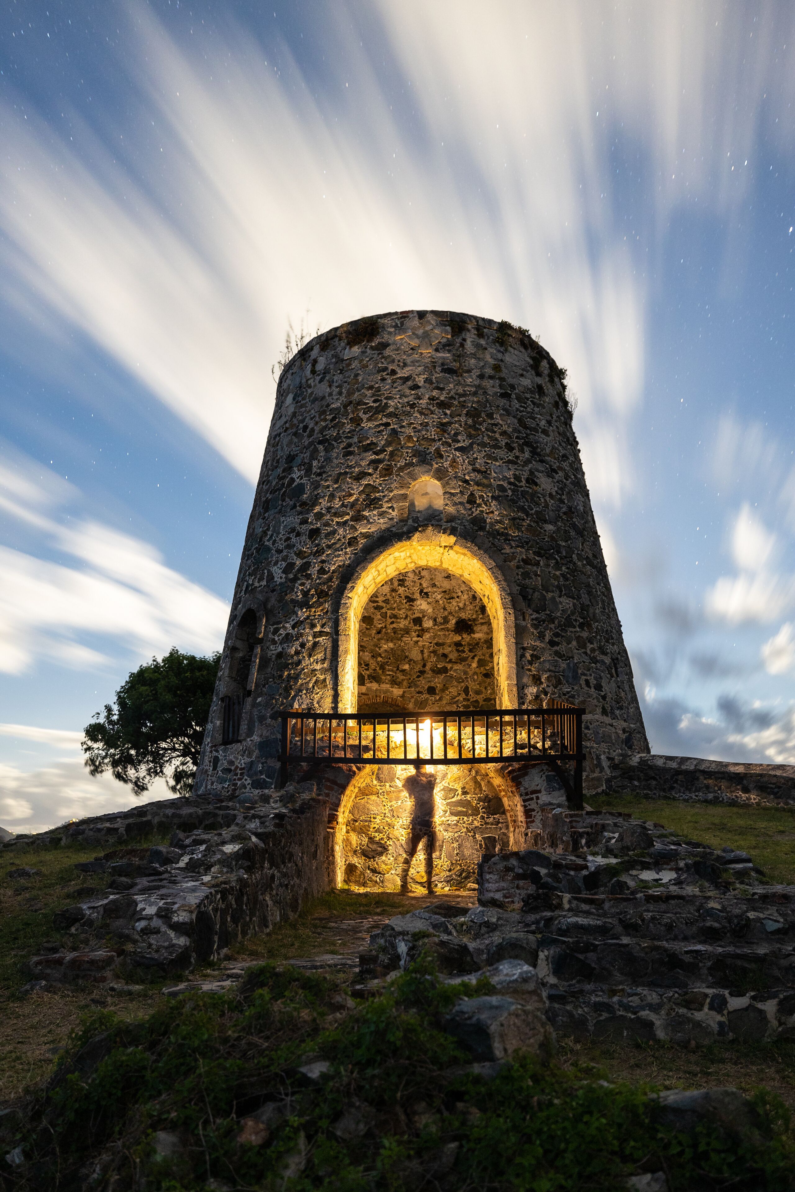 A stone tower with an illuminated archway and a person standing in front.