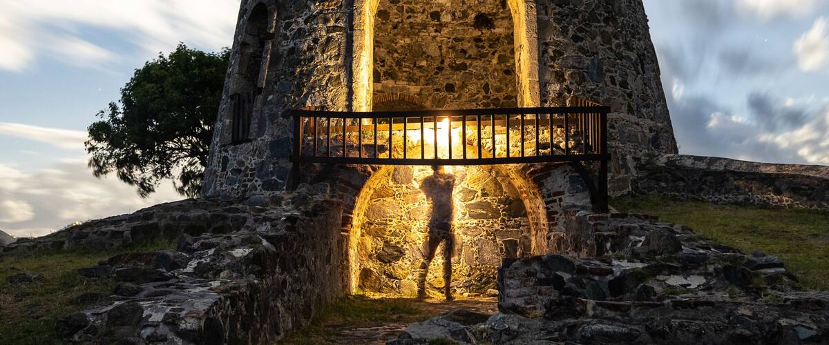 A stone tower with an illuminated archway and a person standing in front.
