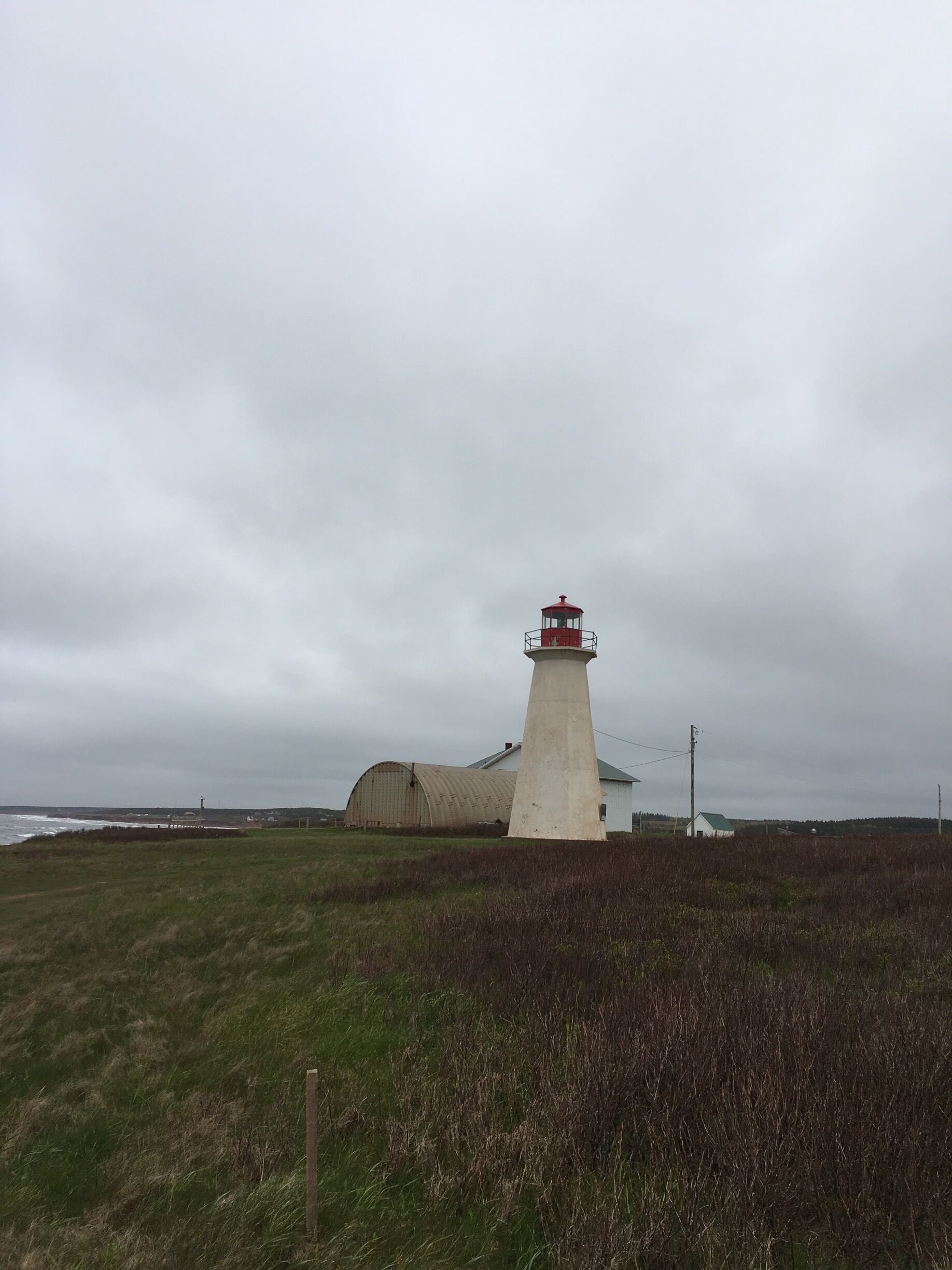 A lighthouse with a red top, a white building, and a grassy field.