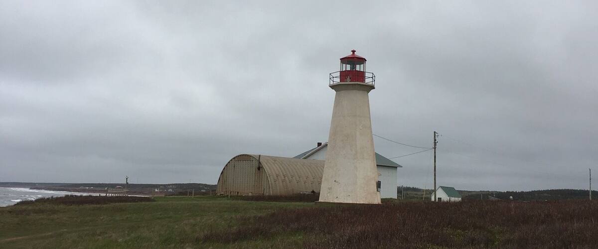 A lighthouse with a red top, a white building, and a grassy field.