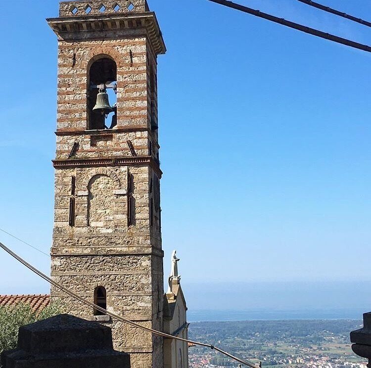 A tall stone tower with a bell, a clock, and a statue at the top.