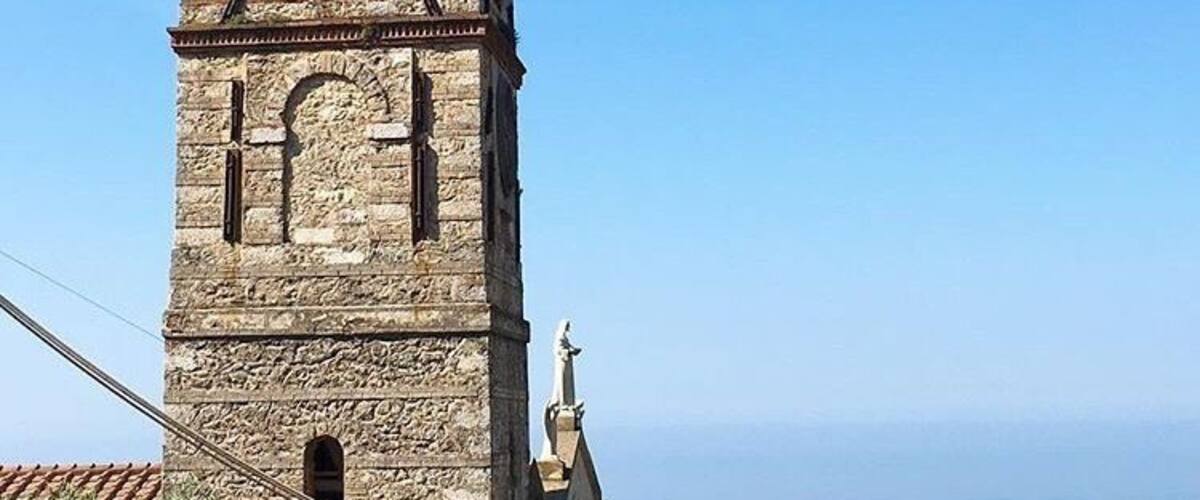 A tall stone tower with a bell, a clock, and a statue at the top.