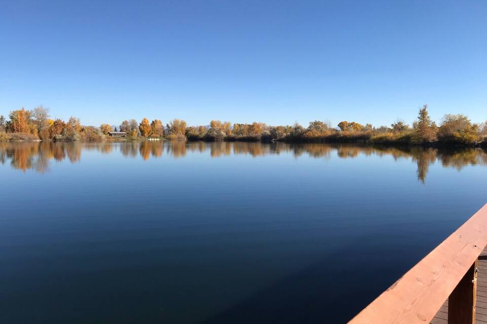 A calm lake with autumn-colored trees and a wooden dock.