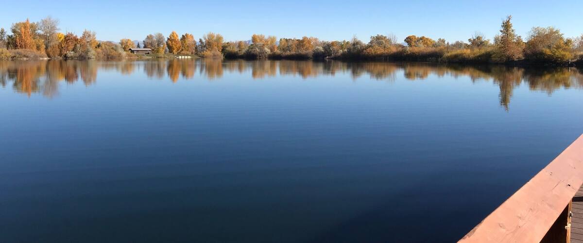 A calm lake with autumn-colored trees and a wooden dock.