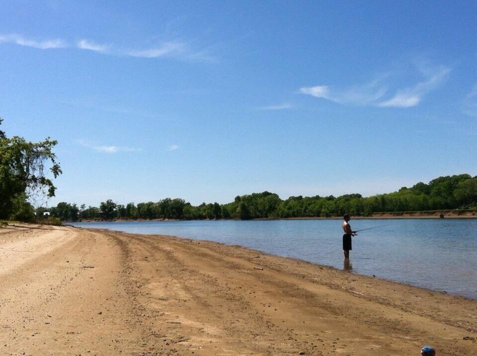 A sandy beach with a person fishing by the water.