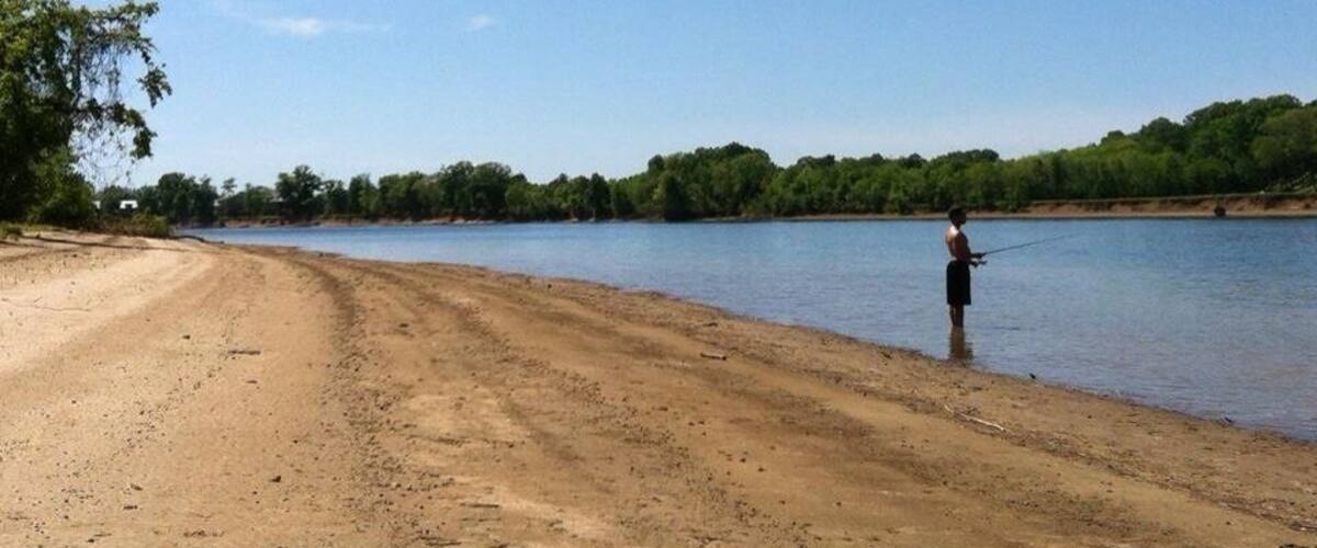A sandy beach with a person fishing by the water.