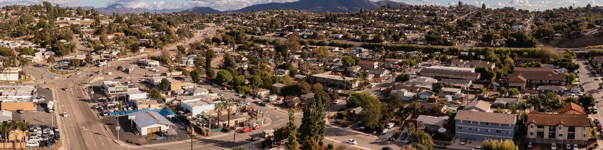 A town with a mountain in the background, a clear sky, and scattered clouds.