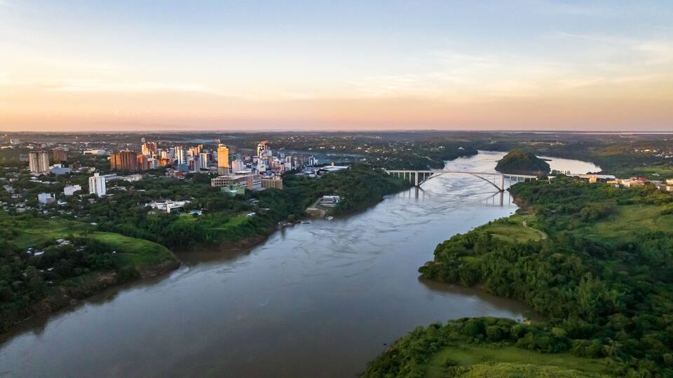 A river flowing through a city with a bridge and dense greenery.