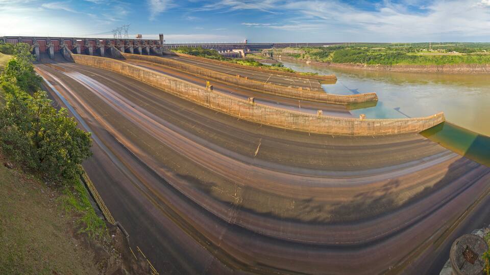 A large dam with multiple spillways and a river flowing through it.