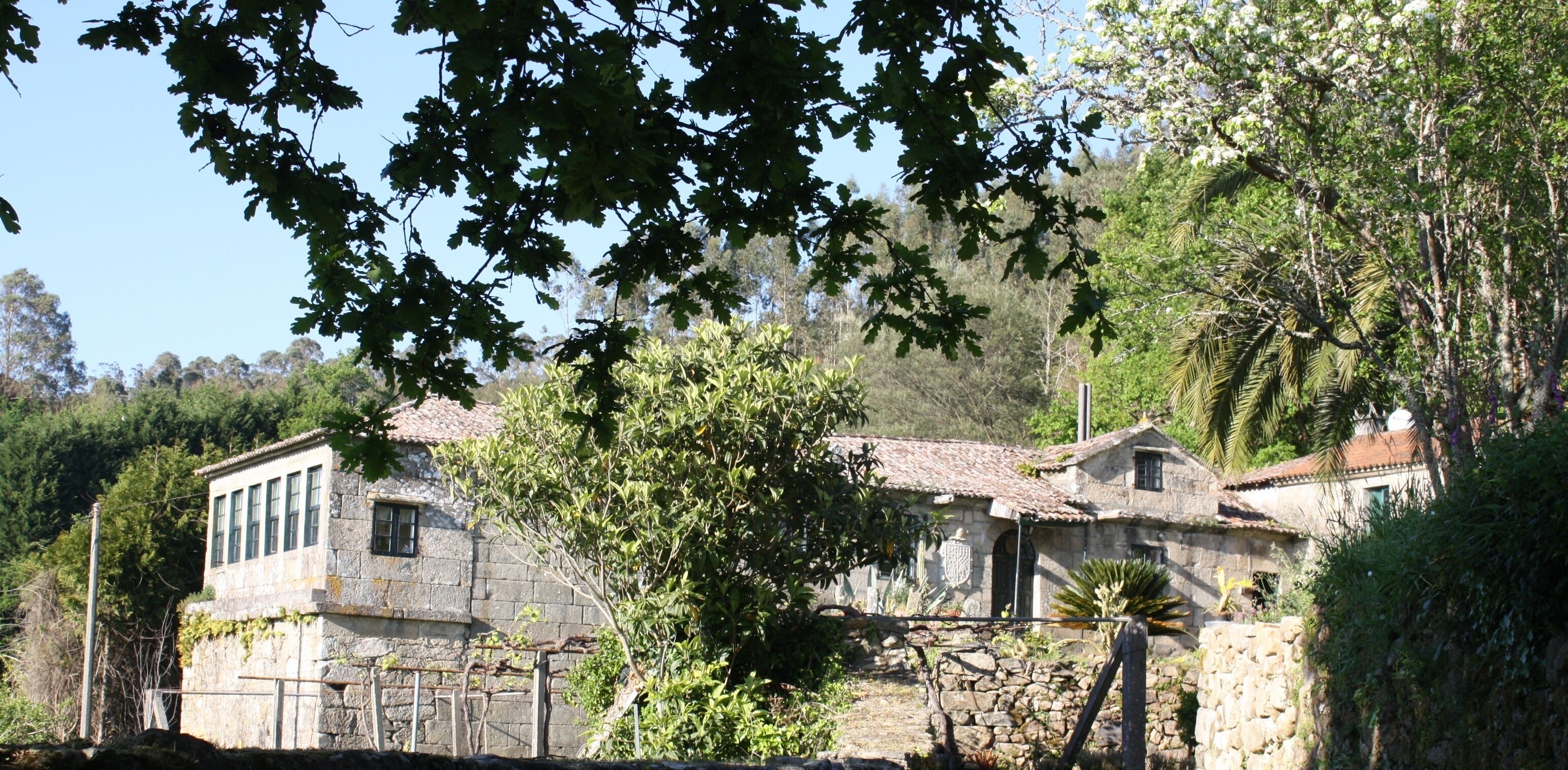 A stone building with a tiled roof surrounded by trees and vegetation.