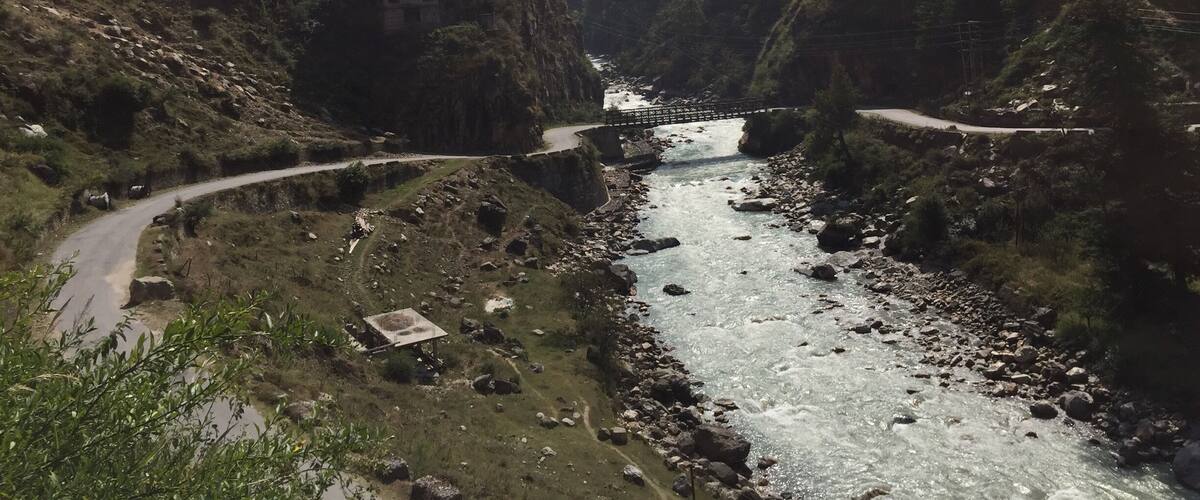 A river flowing through a mountainous valley with a bridge and a winding road.