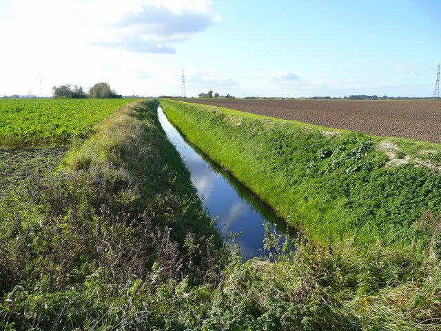 Un estrecho canal de agua bordeado por vegetación y campos verdes.