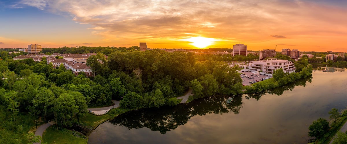 A sunset over a city with a river, surrounded by greenery and buildings.