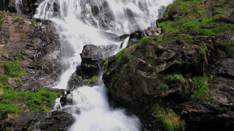 A cascading waterfall surrounded by rocky terrain and green vegetation.