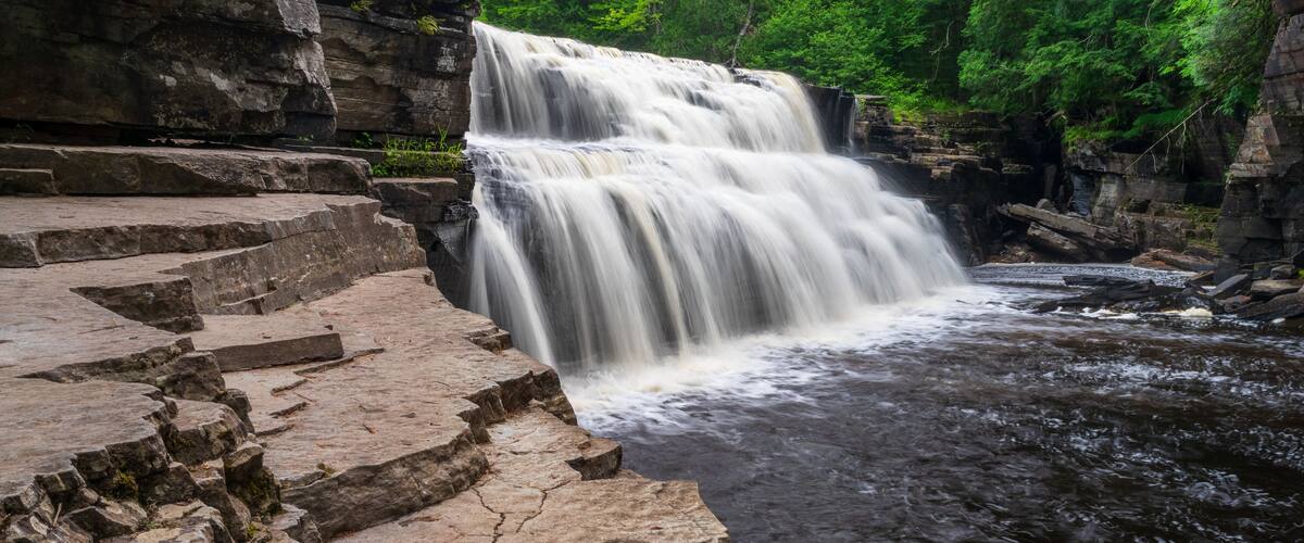 A multi-tiered waterfall cascading over stone steps surrounded by lush greenery.
