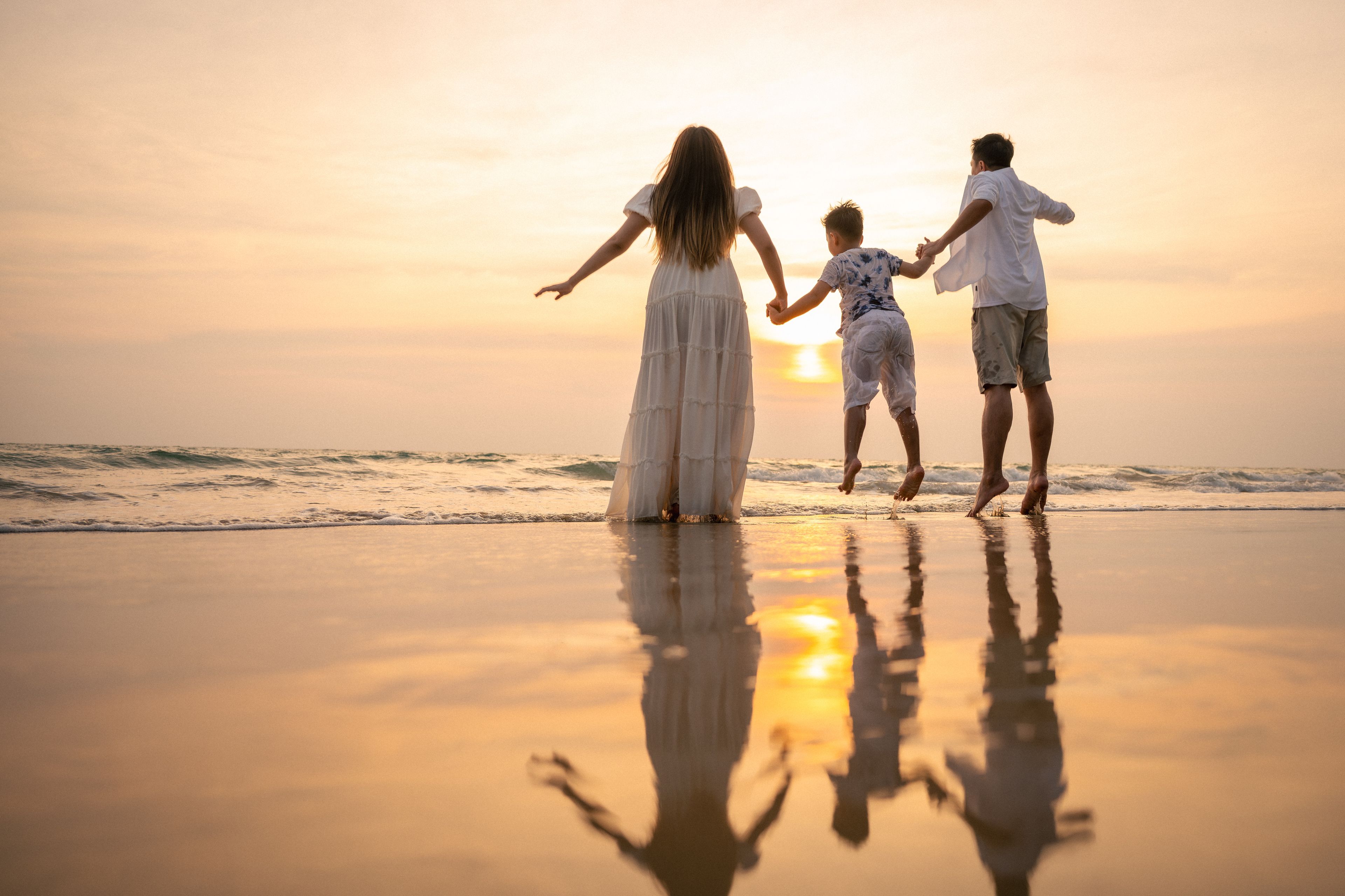 A sunset at the beach with three people holding hands.