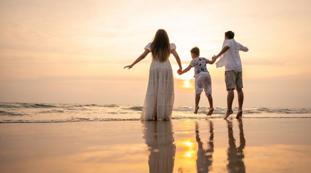 A sunset at the beach with three people holding hands.