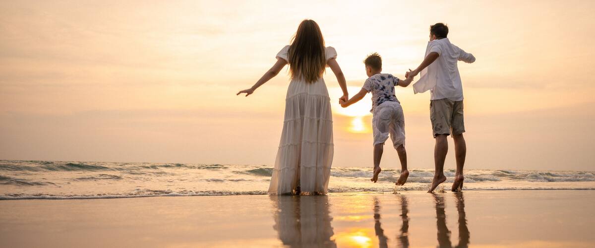 A sunset at the beach with three people holding hands.
