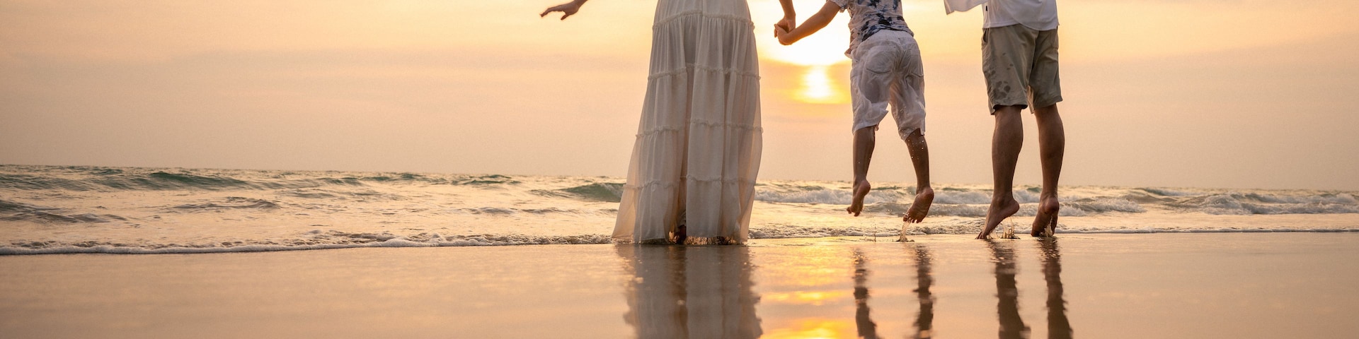 Atardecer en la playa con tres personas tomadas de la mano.