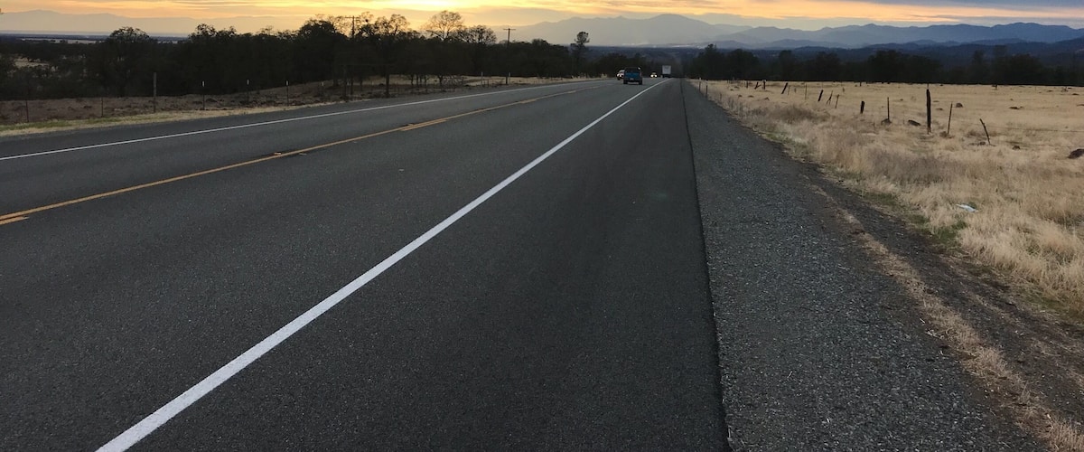 A highway with a sunset in the background and mountains in the distance.