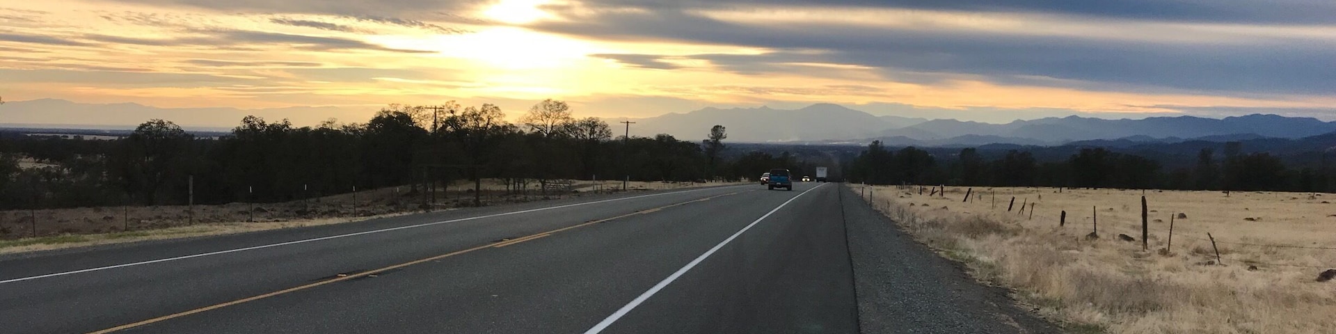 A highway with a sunset in the background and mountains in the distance.
