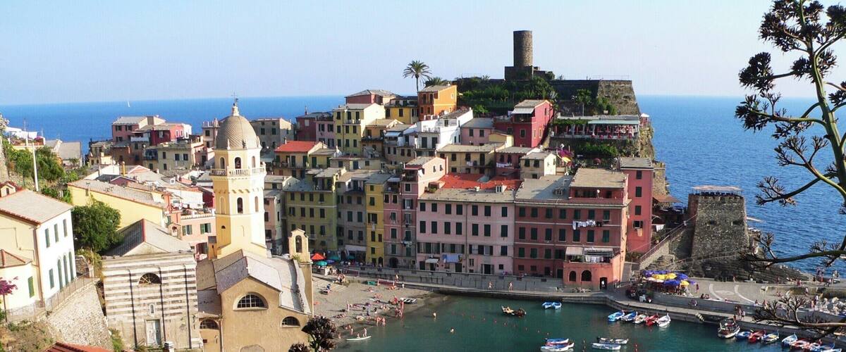 A coastal town with colorful buildings, a prominent church, and a historic tower by the sea.