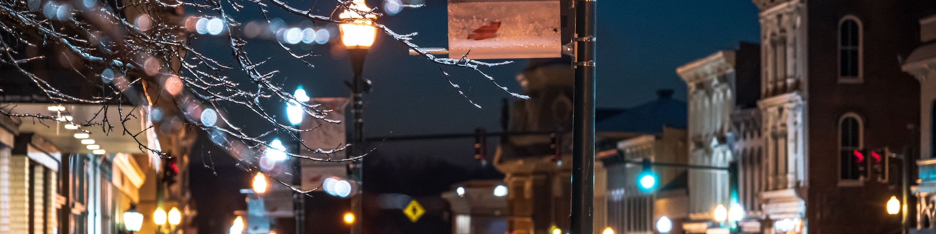 A snow-covered street with a 'Welcome to Georgetown' sign, illuminated street lamps, and historic buildings.