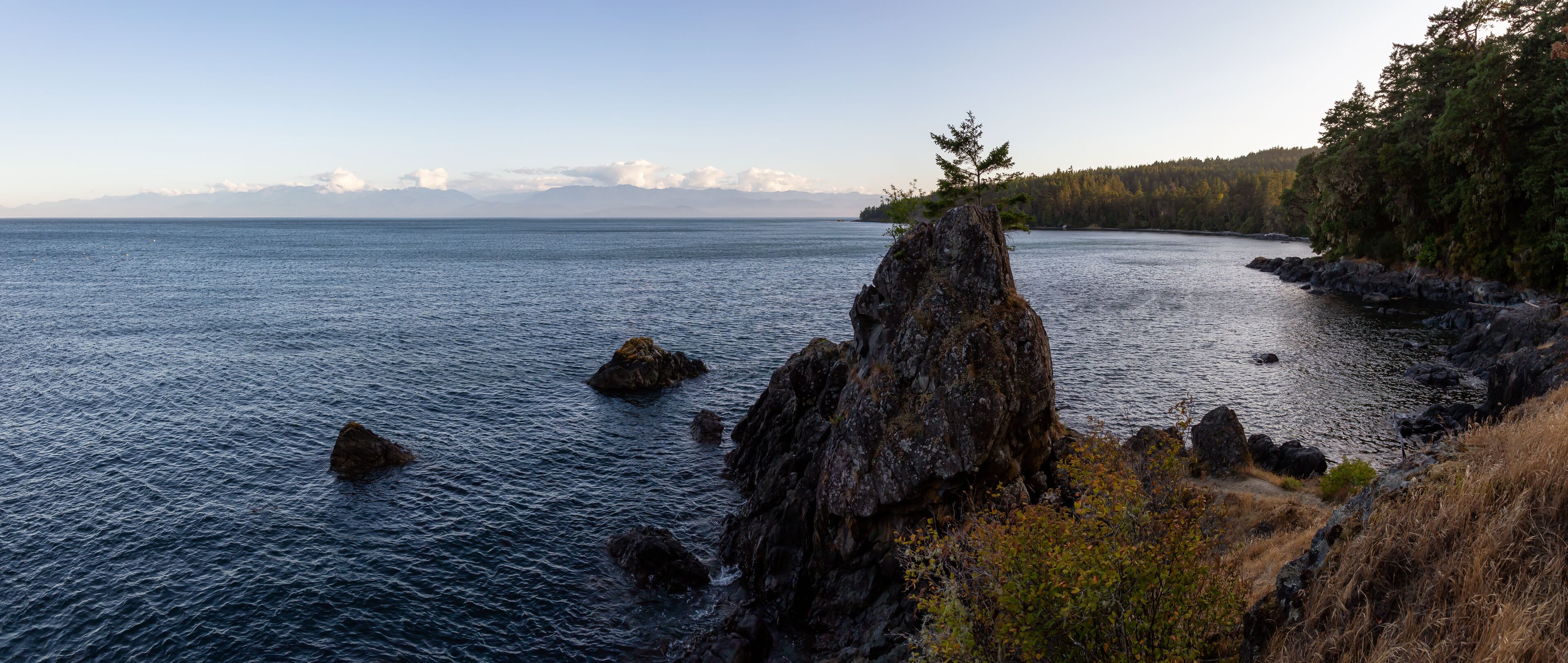 A rocky coastline with a clear view of the sea and distant mountains.