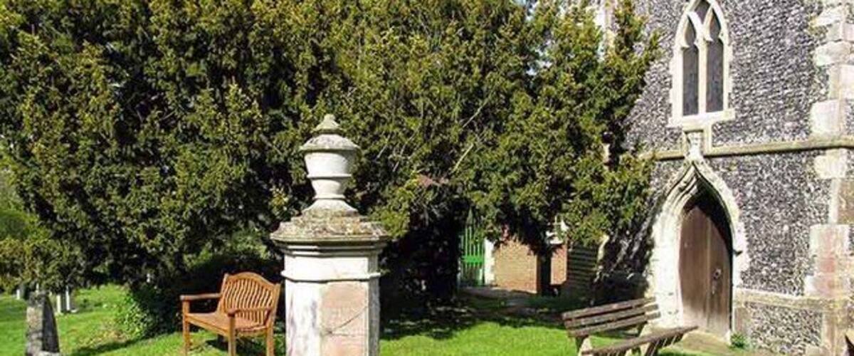 A cemetery with a stone monument, a wooden bench, and a church in the background.