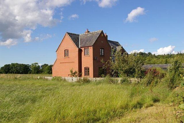 A red brick house with a gabled roof in a grassy field.