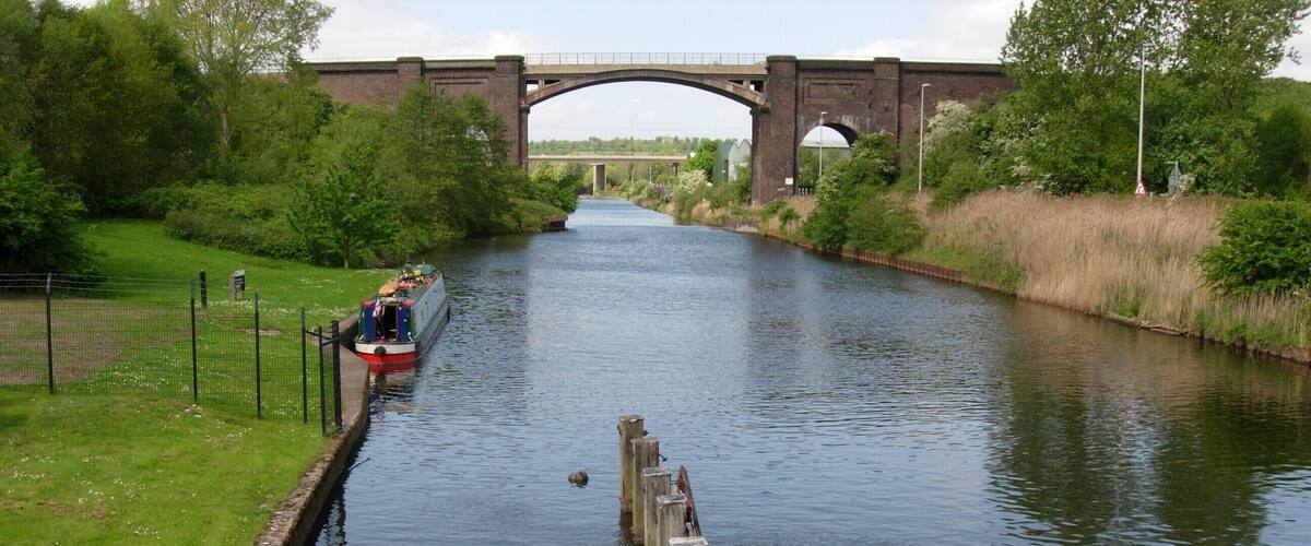 A narrow canal with a boat, a bridge, and greenery.