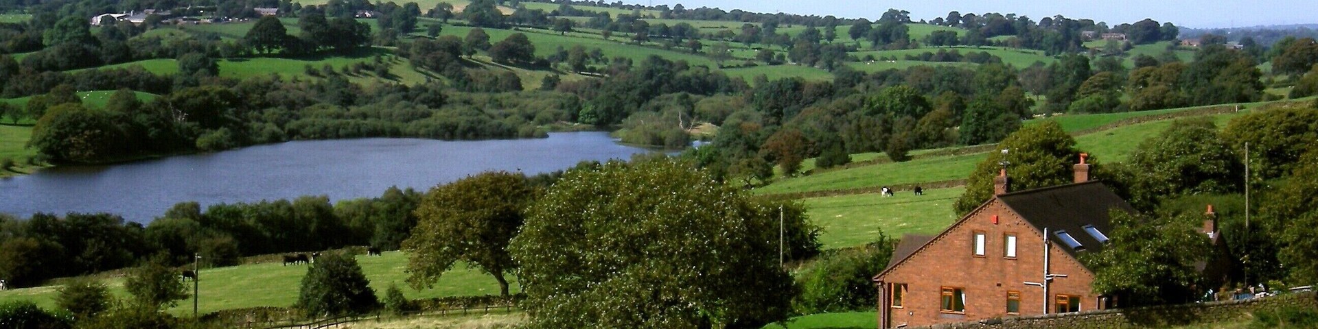 Un paisaje rural con un lago, colinas onduladas y una casa de ladrillo.