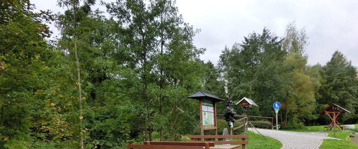 A picnic area with wooden benches and tables, surrounded by greenery and a cobblestone path.