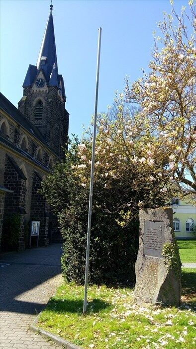 A church with a tall spire, a stone monument, and a flowering tree.