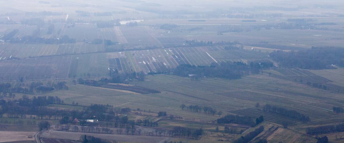 A vast agricultural landscape with fields and scattered trees.