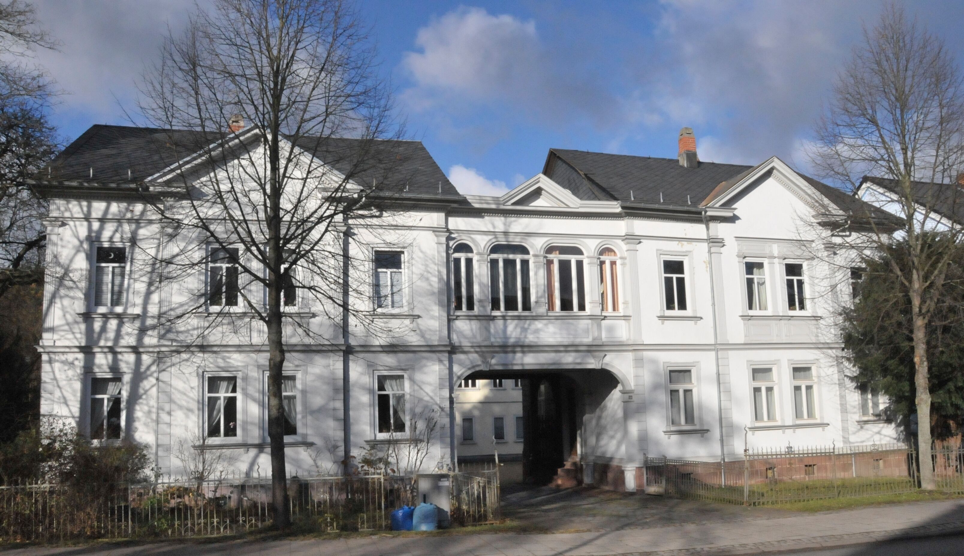 A large, white, two-story building with a symmetrical facade, multiple windows, and a central archway.