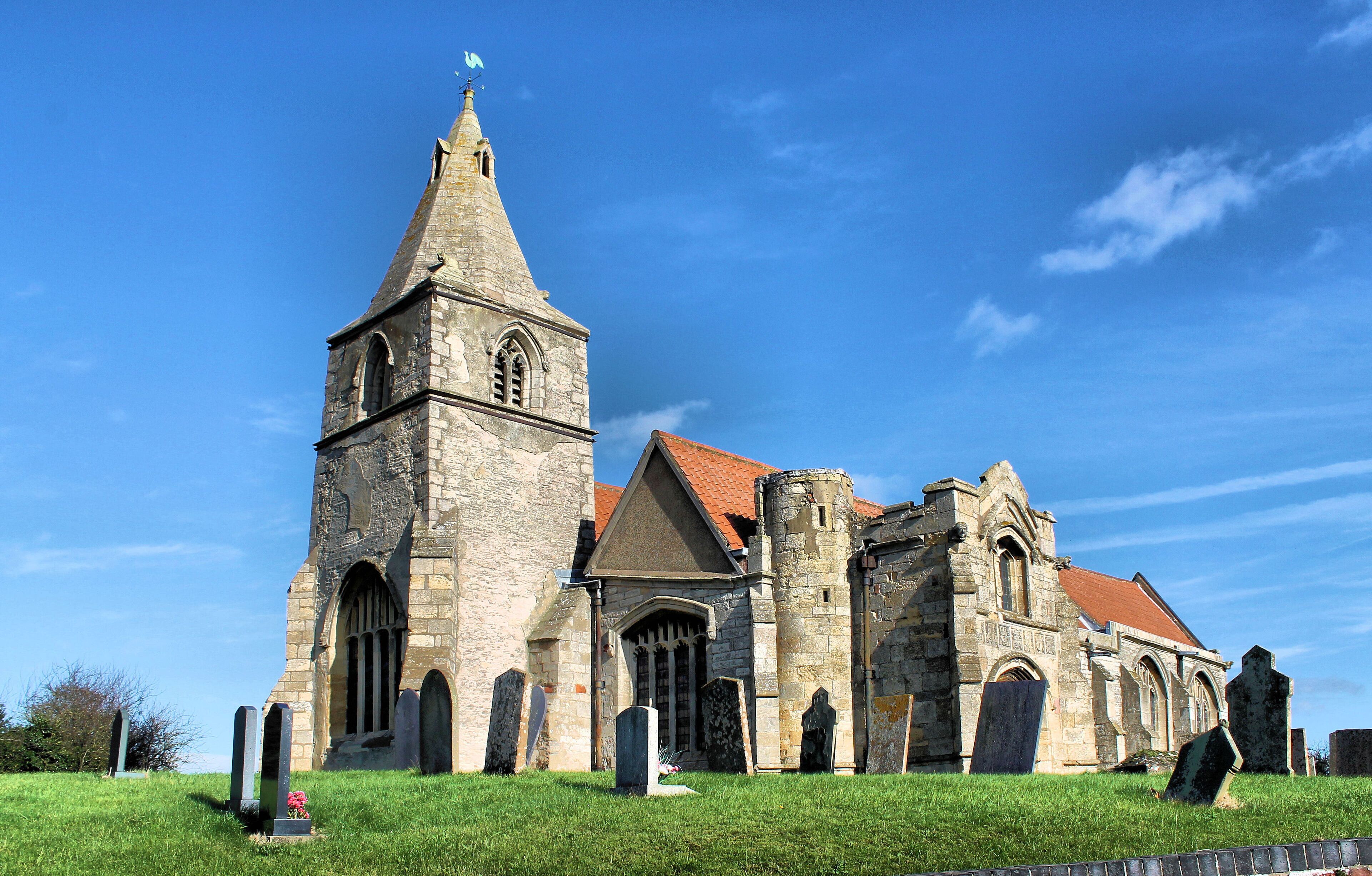 A historic church with a tall tower and multiple arches, surrounded by a cemetery.