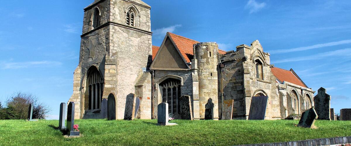 A historic church with a tall tower and multiple arches, surrounded by a cemetery.